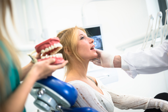 Young woman in dental chair looking at dentures