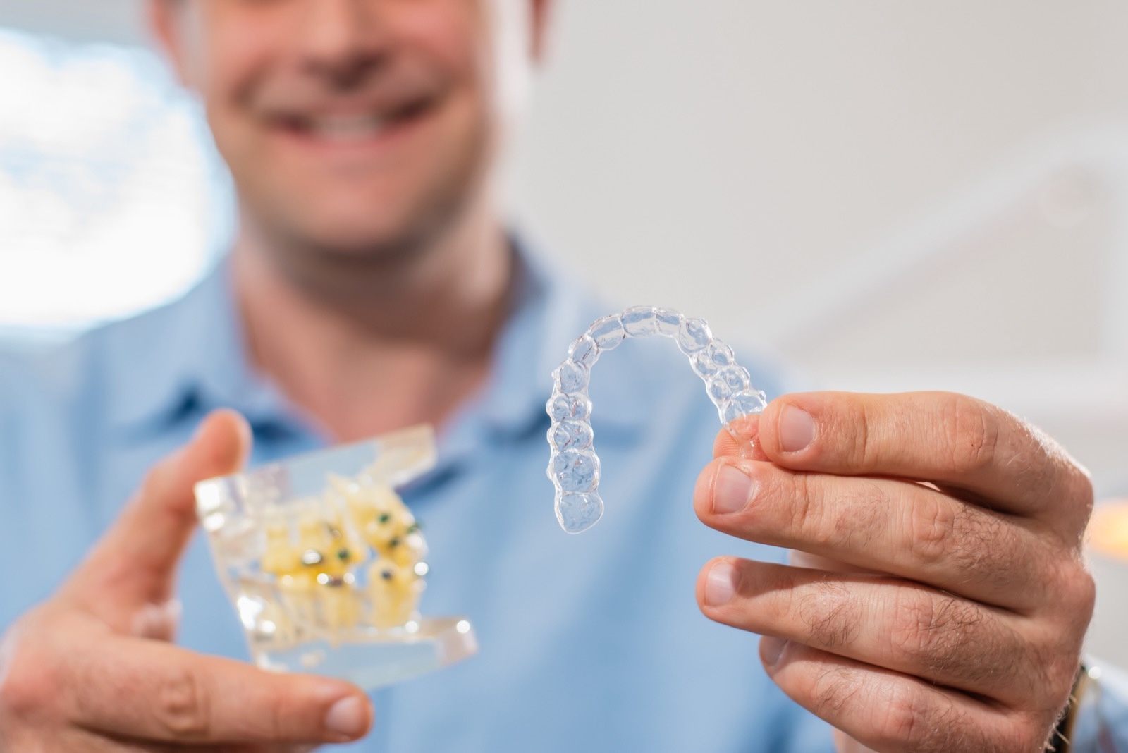 Dental care.Smiling dentist doctor holding aligners and braces in hand shows the difference between them